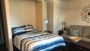 Un dormitorio con una cama, un sofá, una mesita de noche, una lámpara y un adorno en la pared.