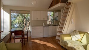 A compact kitchen with white cabinets, a dining table with chairs, a staircase, and a sofa with a patterned throw. - A delightful studio in idyllic Mapua Village, perfect from which to explore the Tasman region (Mapua)