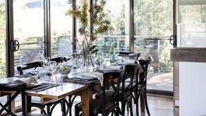 Comedor con mesa de madera dispuesta para cuatro personas, rodeada de sillas negras, bajo una lámpara colgante.