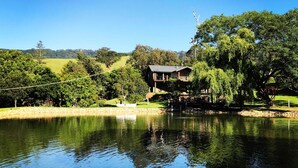 Una propiedad junto al lago con una casa de madera, rodeada de exuberante vegetación y un cielo azul despejado.