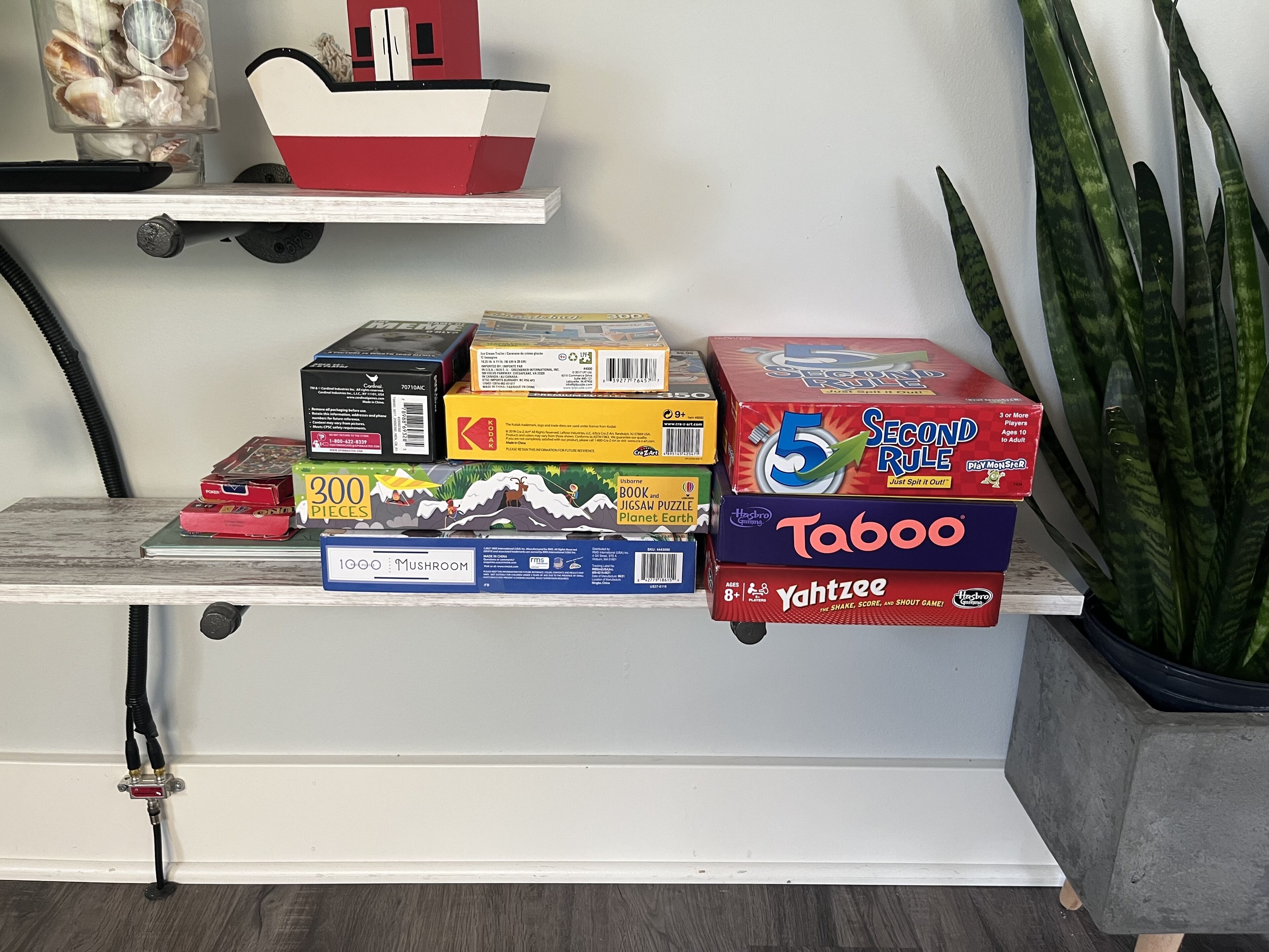 Ein Regal mit verschiedenen Brettspielen und Puzzles, darunter 'Taboo' und '5 Second Rule'.