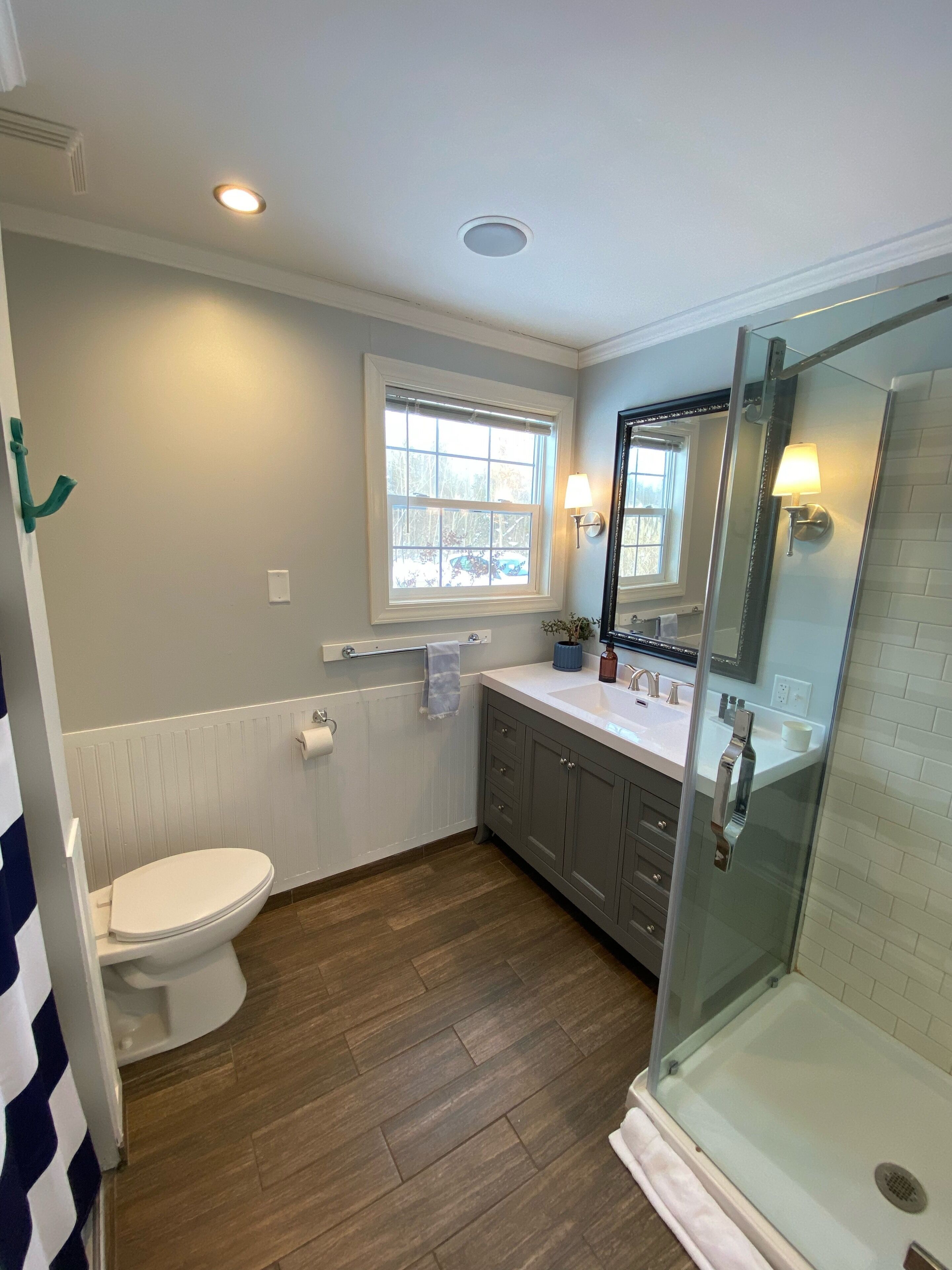 Une salle de bain comprenant des toilettes, une fenêtre, un lavabo avec un miroir et un espace douche.