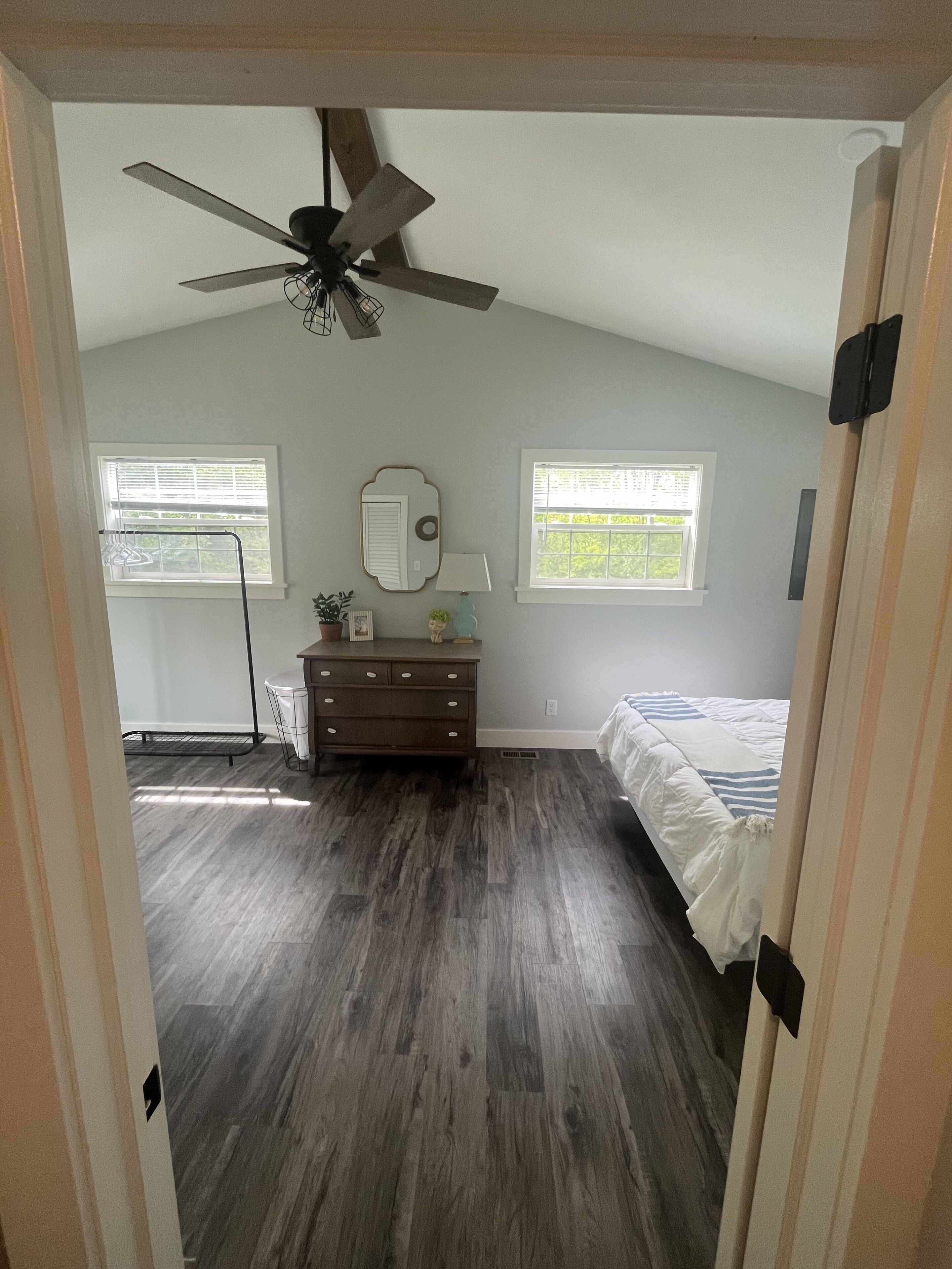 A bedroom with a ceiling fan, a dresser, a bed, and two windows.