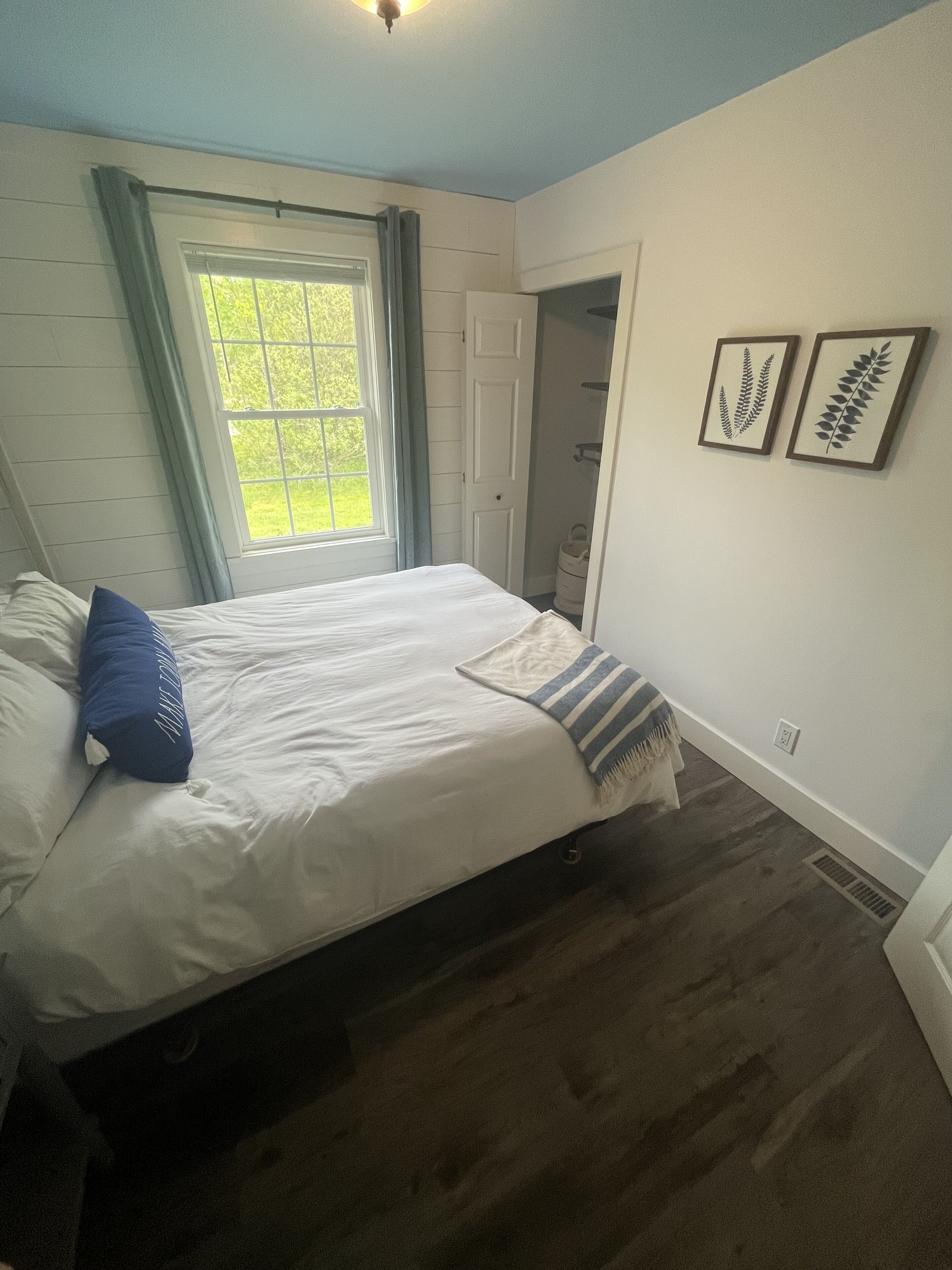 A bedroom with a bed, a window, a door, and two framed leaves on the wall.