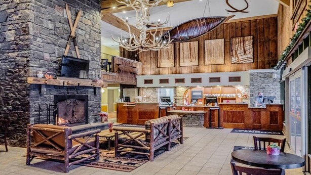 A rustic interior with a stone fireplace, wooden ceiling beams, a bar area, and a hanging antler chandelier. - Hot SKI-in SKI-out Rentals Bentley Brook Resort! (Hancock)