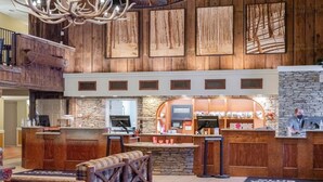 A rustic lobby with a stone fireplace, wooden reception desk, and a seating area with a checkered bench. - Hot SKI-in SKI-out Rentals Bentley Brook Resort! (Hancock)