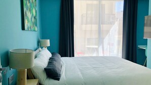 A hotel room with a bed, a lamp, a painting on the wall, and a view of the outside balcony. - Sliema Beach Apartment (Sliema)