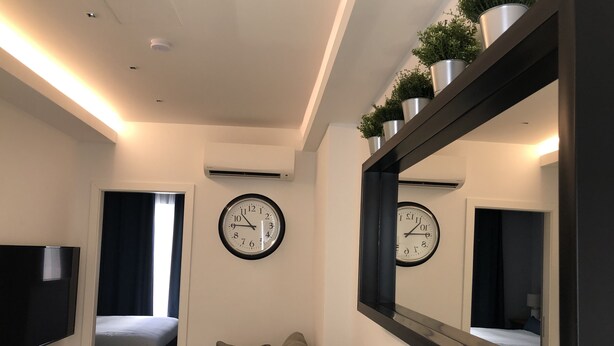 A modern hotel room with a sofa, two wall clocks, a TV, and a mirror. - Sliema Beach Apartment (Sliema)