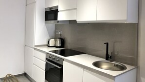 A modern kitchen with white cabinets, a stainless steel sink, a built-in oven, a microwave, and a toaster. - Sliema Beach Apartment (Sliema)