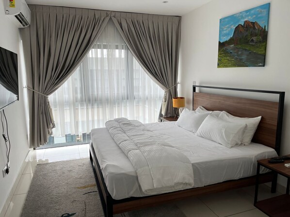 A hotel room with a large bed, a wooden headboard, a painting on the wall, and a window with curtains.