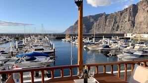 A wooden deck with a table set for two, overlooking a marina with numerous boats docked. - Luxury and functional sea view apartment (Los Gigantes)