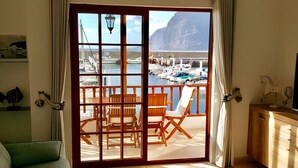 A room with a sliding glass door leading to a balcony with wooden furniture and a view of a marina. - Luxury and functional sea view apartment (Los Gigantes)
