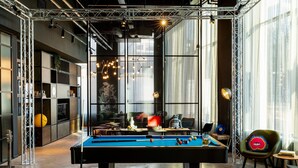 A pool table in a modern room with a large window, a sofa, and a chair.