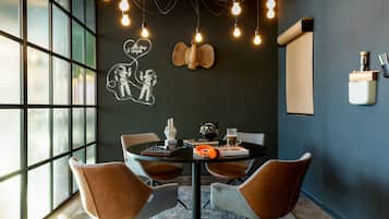 Un espace de salle à manger moderne avec une table ronde, quatre chaises et un mur décoratif agrémenté d’un lustre en forme d’ampoule.