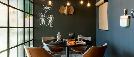 A modern dining area with a round table, four chairs, and a decorative wall with a light bulb chandelier.