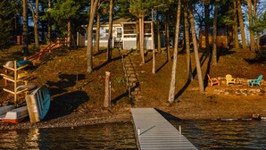 Un chalet au bord du lac, doté d’un quai, entouré d’arbres et offrant un espace de détente extérieur.