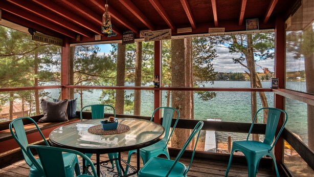 Une terrasse couverte avec une table ronde et des chaises, donnant sur un lac.