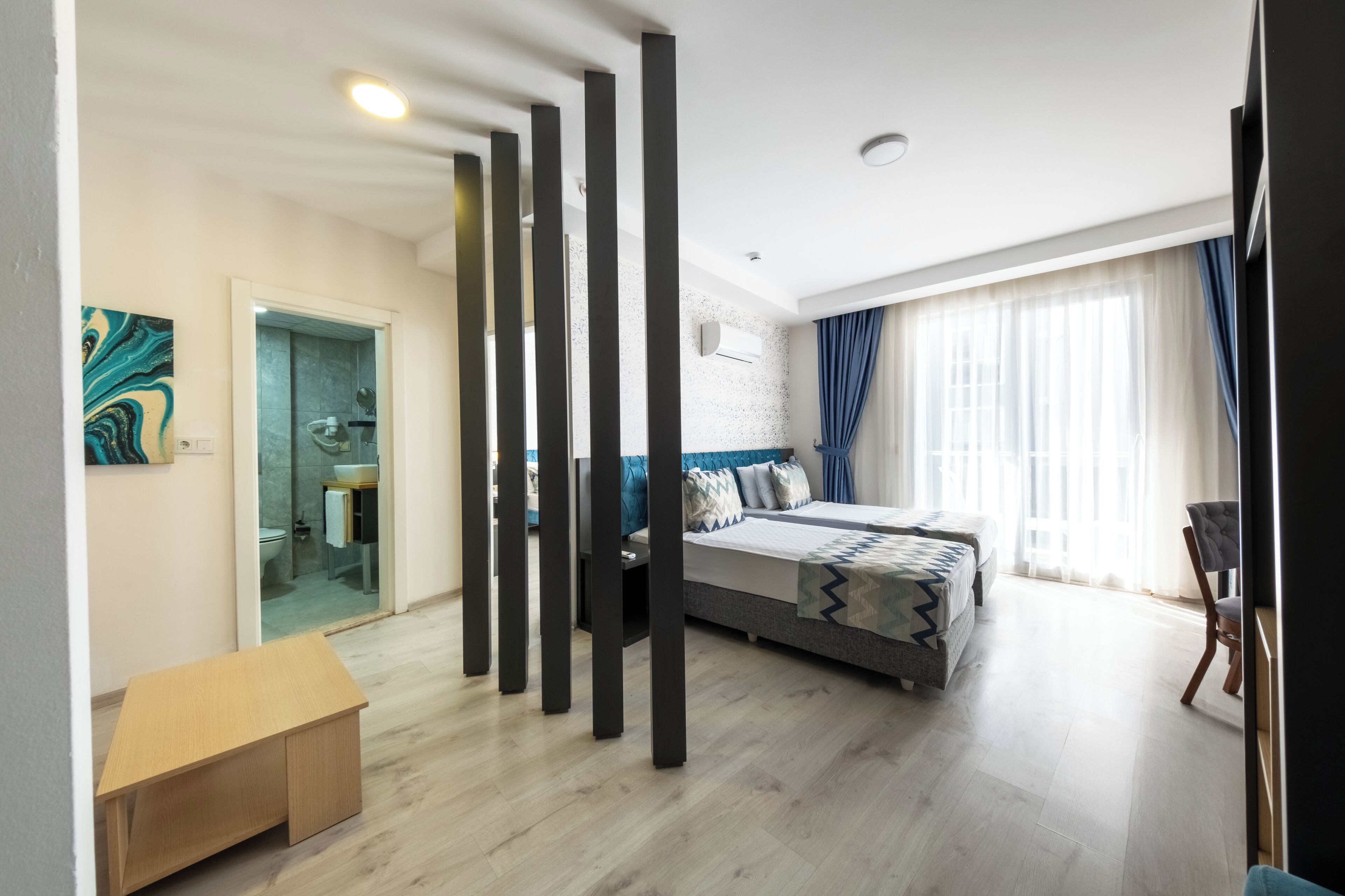 Un dormitorio moderno con una cama, un escritorio y un baño visible a través de una puerta de cristal.