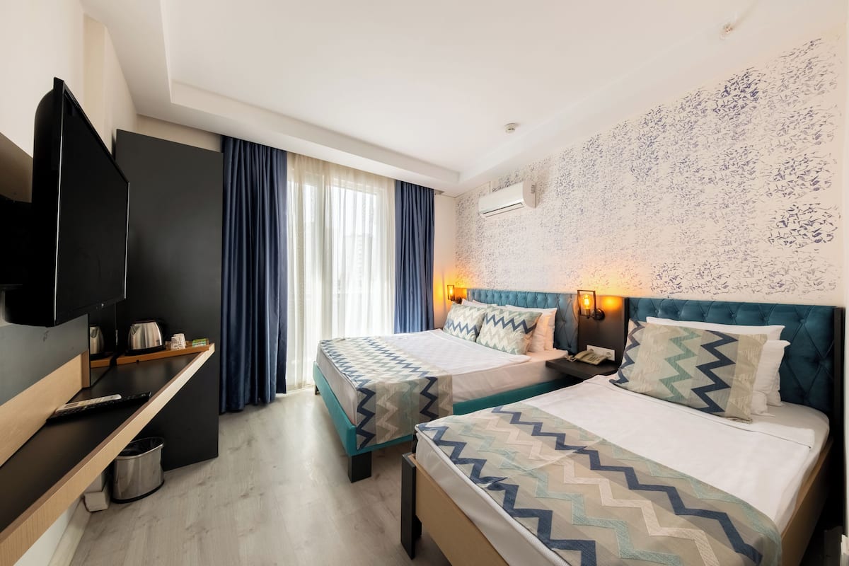 A hotel room with two beds, a TV, a desk, and a window with curtains.