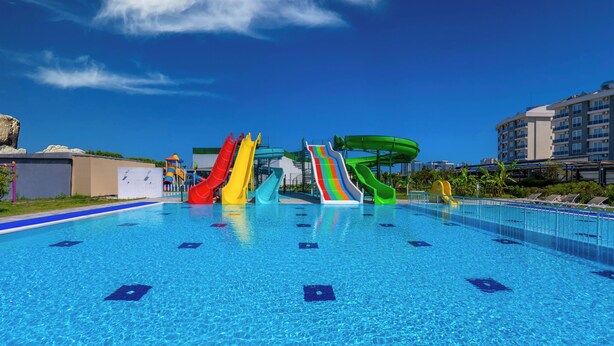 A swimming pool with multiple colorful slides and a clear blue sky. - Palmora Lara Hotel - All inclusive (Antalya)