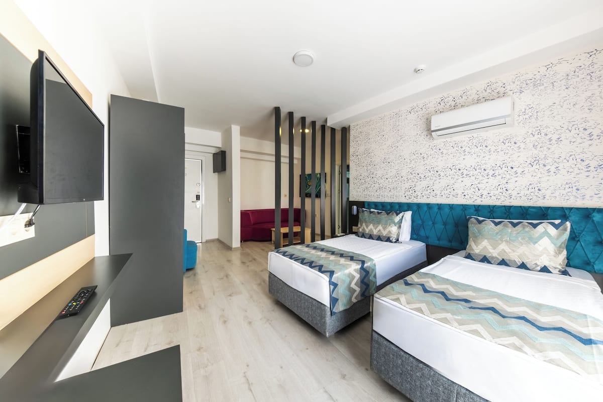 A modern hotel room with two beds, a flat-screen TV, and an air conditioning unit on the wall.