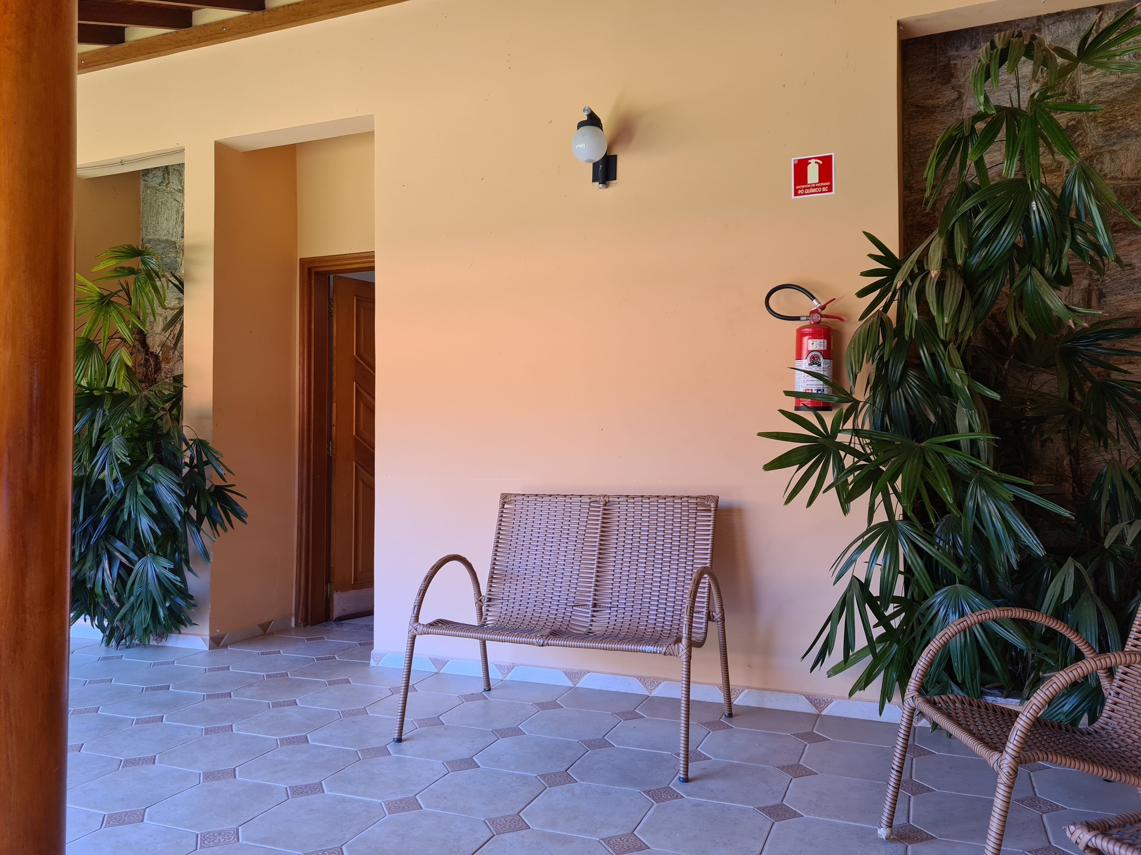 A covered outdoor area with hexagonal tiles, a wicker chair, and a fire extinguisher mounted on the wall.