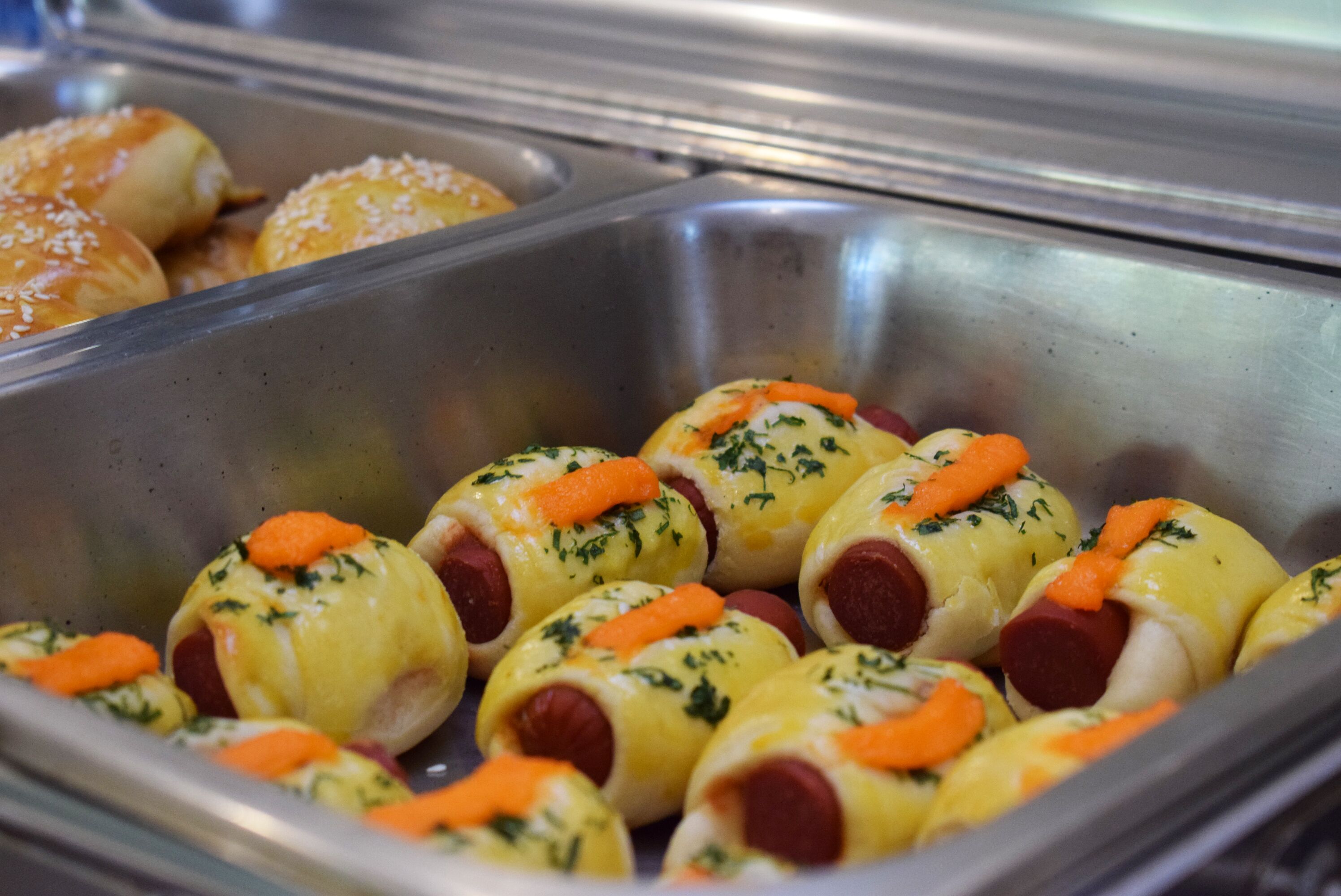 A buffet with various food items including rolls and sausage rolls garnished with herbs and carrots.