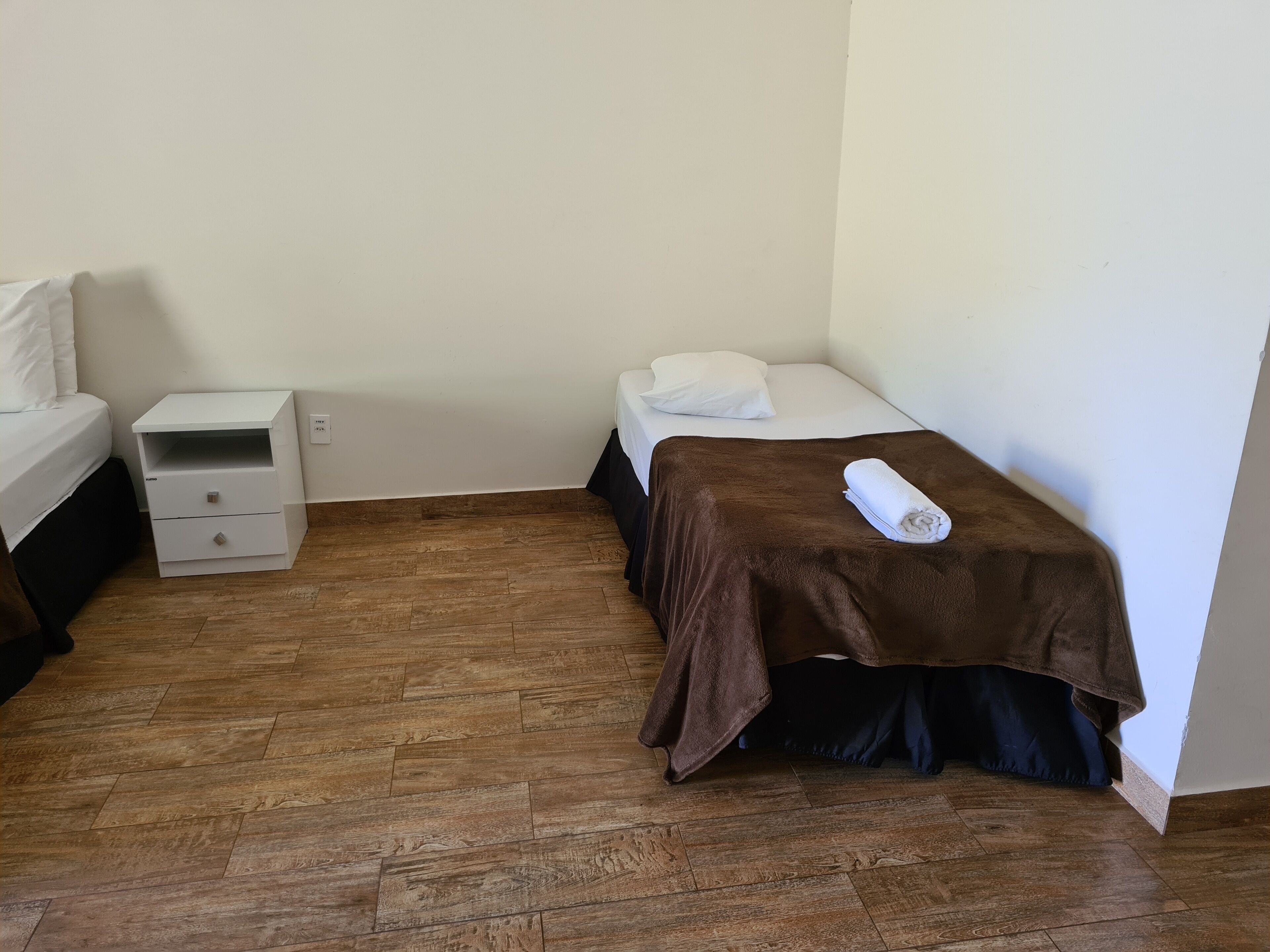 A small, neatly arranged room with a bed, a nightstand, and a wooden floor.