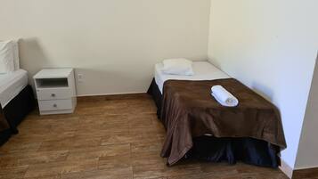 Um quarto pequeno e bem organizado, com uma cama, uma mesinha de cabeceira e piso de madeira.