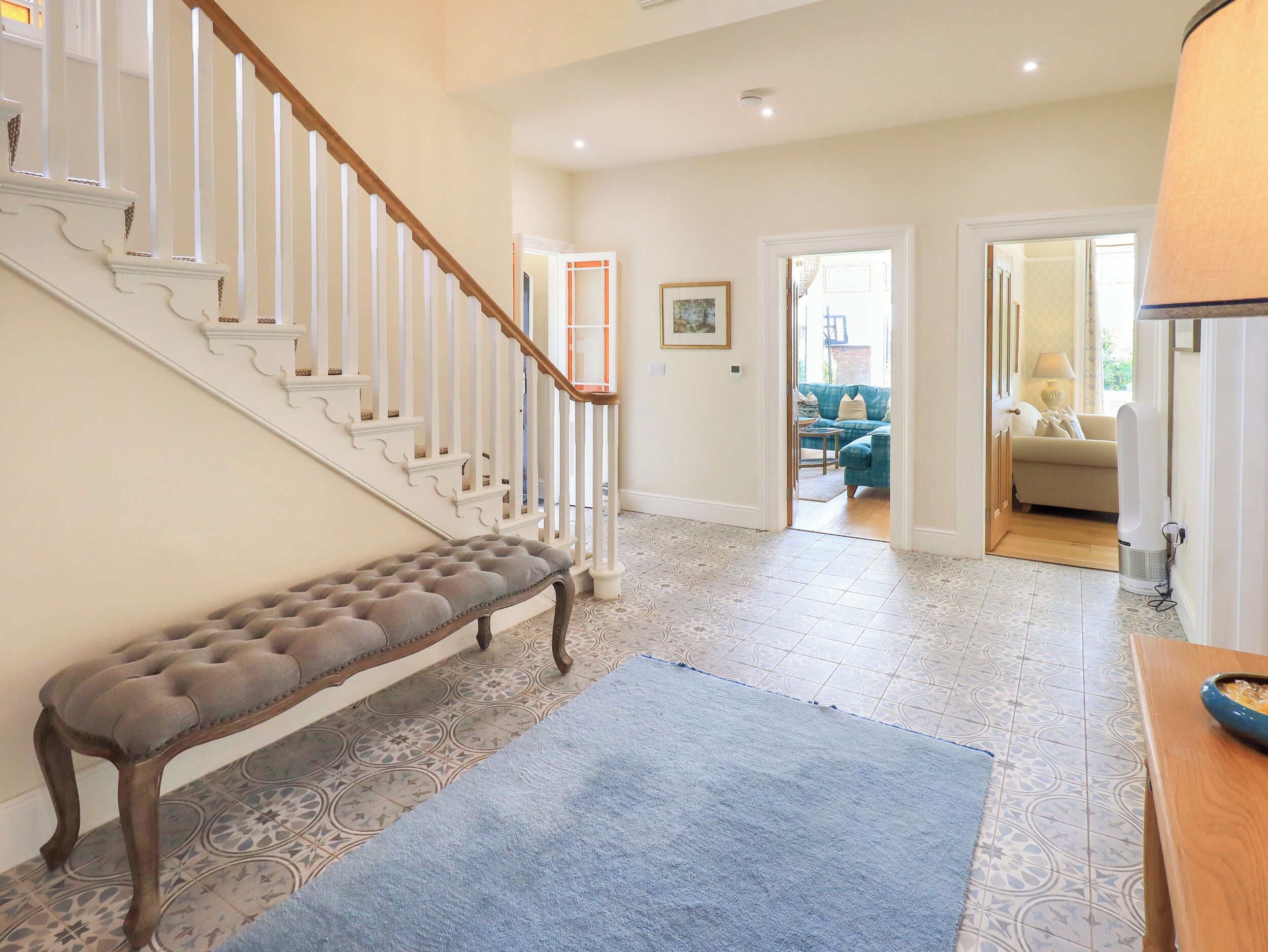 Un escalier avec des balustrades blanches, un banc capitonné, des carreaux de sol à motifs et un tapis bleu.