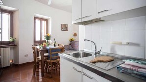 A modern kitchen with white cabinets, a stainless steel sink, and a dining area with a table and chairs. - Corallo studio mezzanine (Spello)