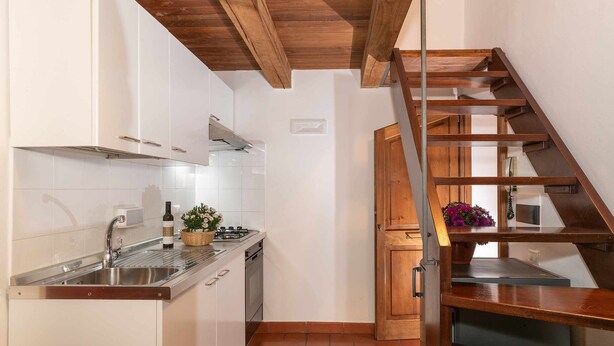 A kitchen with white cabinets, a stainless steel sink, and a wooden staircase. - Corallo studio mezzanine (Spello)