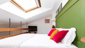A bedroom with a skylight, a bed with white and red bedding, a green accent wall, and a TV on a stand. - Corallo studio mezzanine (Spello)