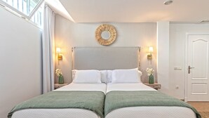 Una cama doble con dos almohadas, un espejo redondo arriba y dos mesitas de noche con lámparas y jarrones.