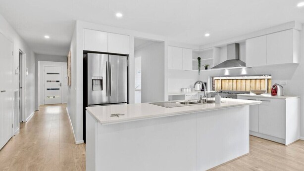A modern kitchen with white cabinetry, a stainless steel refrigerator, a built-in stove, and a large island with a sink. - OSCAR -  A Tranquil Armstrong Creek Home + NETFLIX (Armstrong Creek)