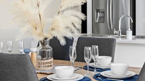 A dining table set with white plates, bowls, and glasses, a vase with pampas grass, and a modern kitchen in the background. - OSCAR -  A Tranquil Armstrong Creek Home + NETFLIX (Armstrong Creek)