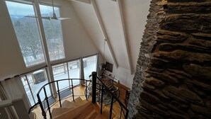 Ein Zimmer mit hohen Decken, einer Steinsäule, einer Wendeltreppe und großen Fenstern mit Blick auf eine verschneite Landschaft.