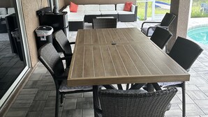 Un patio couvert comprenant une table et des chaises, un canapé avec des coussins, un ventilateur de plafond et une vue sur une piscine.