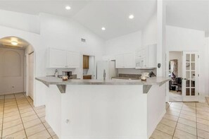 Une cuisine spacieuse avec des meubles blancs, un îlot central et un éclairage encastré.