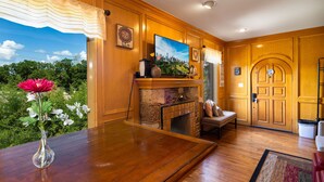 A room with wooden paneling, a fireplace, a large window with a view of greenery, and a door with a decorative glass panel. - 《Best Austin Location ❤Huge Patio w HEATED Cowboy Pool & 65" TV❤ Skyline Views》 (Austin)