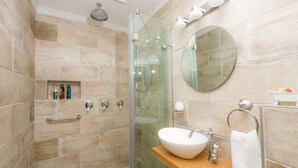 A modern bathroom with a glass-enclosed shower, a wooden vanity with a white sink, and a round mirror on the wall.