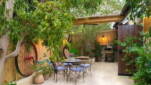 A patio with a round table and chairs, surrounded by potted plants and a wooden fence.