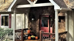 A rustic cabin with a steeply pitched roof, a front porch with wooden railings, and a brick facade.