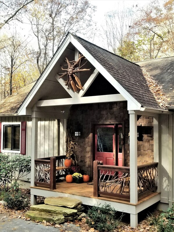 A rustic cabin with a steeply pitched roof, a front porch with wooden railings, and a brick facade.