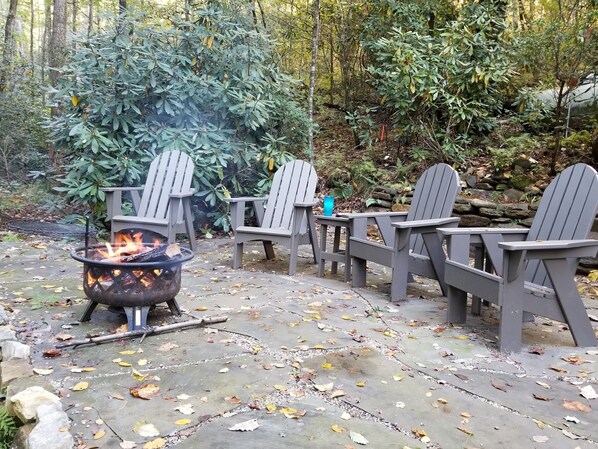 A fire pit with chairs arranged around it in a forested area. - Cozy Creekside Cottage - RELAX by the Creek (Sapphire)