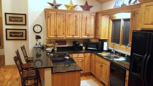 A kitchen with wooden cabinets, a black countertop, a kettle, and a refrigerator.
