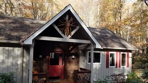 A cabin with a red door, a porch with wooden railings, and a small shed with red shutters.