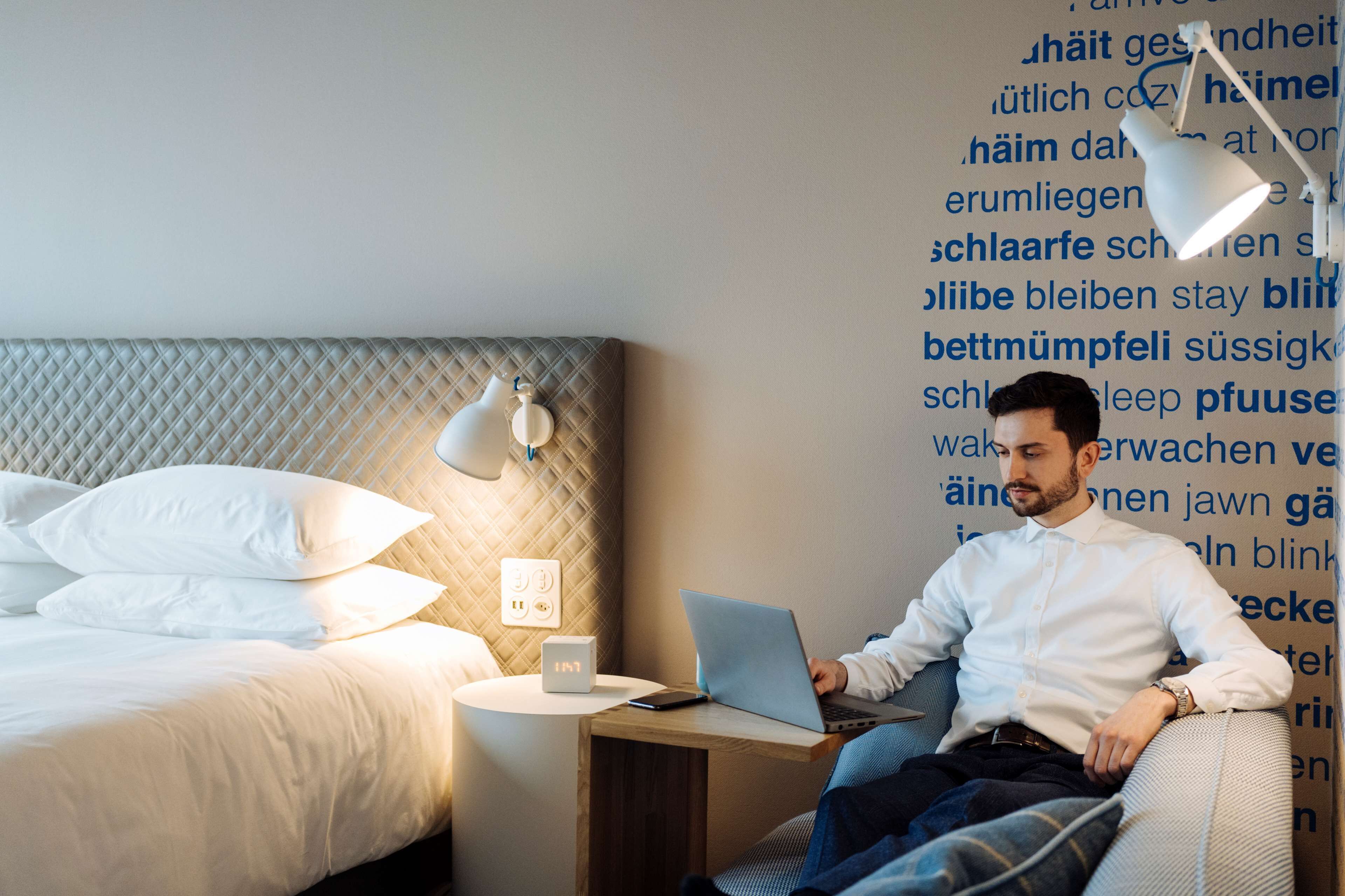 Une chambre d’hôtel avec un lit, une lampe de chevet, un ordinateur portable et une horloge murale.