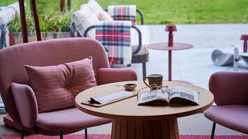 A cozy seating area with a round wooden table, a red patterned sofa, and a matching armchair.