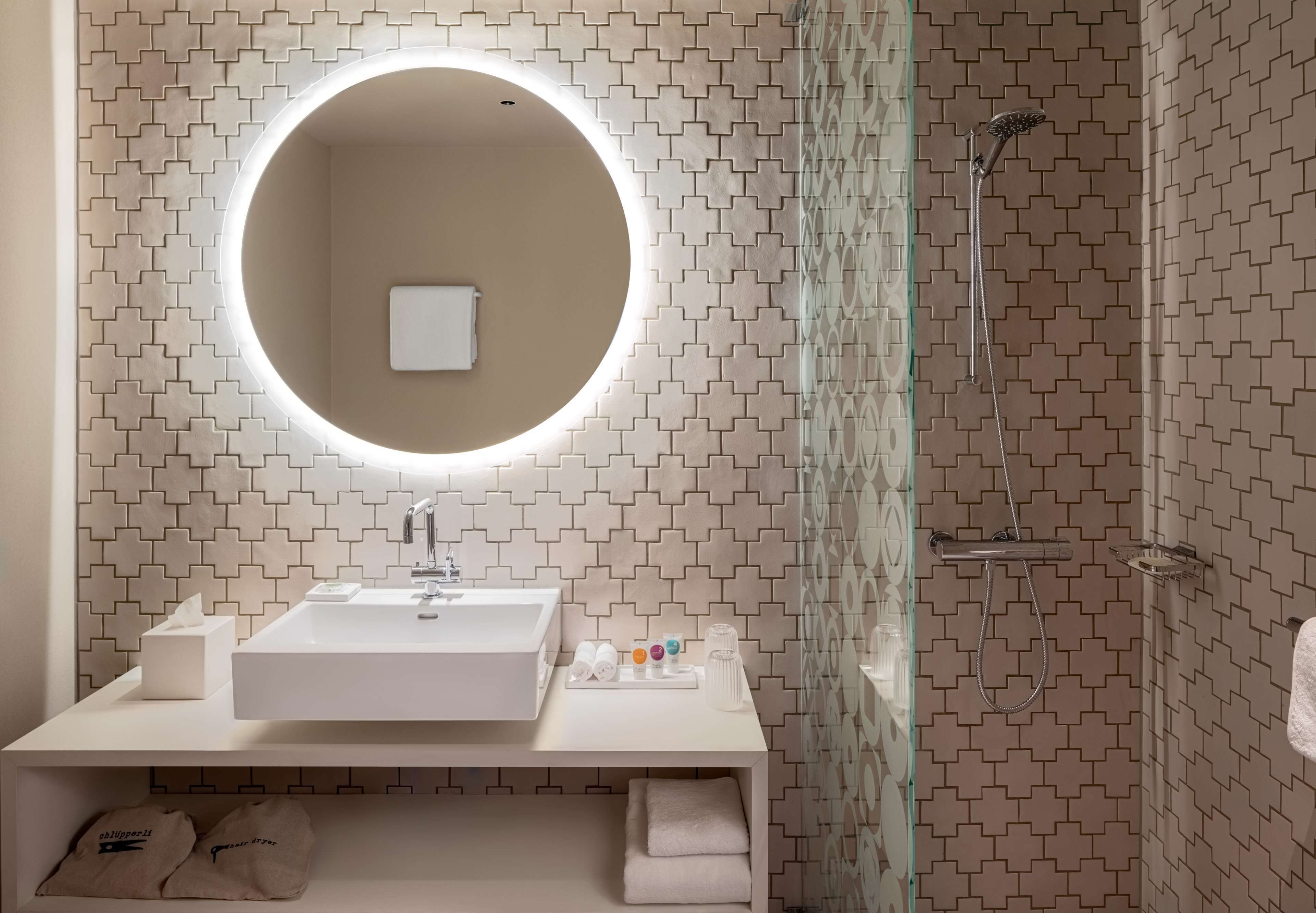 Un baño moderno con un espejo redondo, lavamanos blanco y ducha.